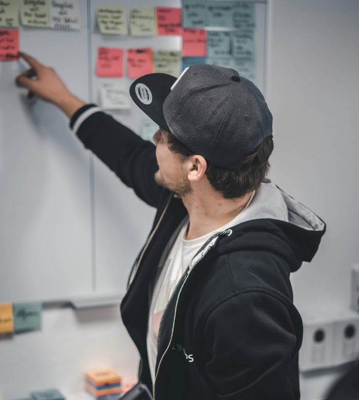 Julian zeigt an einem Whiteboard auf eine Haftnotiz bei der Projektplanung